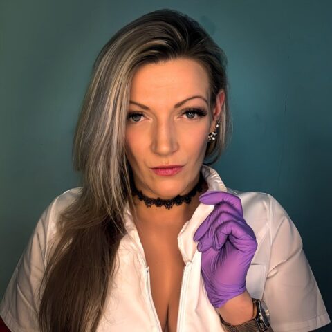 Person mit langen Haaren, weißem Oberteil und violetten Handschuhen, die vor blauem Hintergrund direkt in die Kamera blickt.