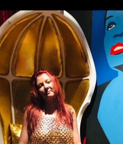 Eine Frau sitzt auf einem goldenen Stuhl vor einem Gemälde.