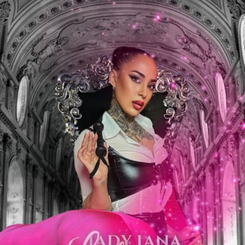 Eine Person in einer Mischung aus gotischer und moderner Kleidung steht vor einem verzierten architektonischen Hintergrund. Im Vordergrund steht inmitten von rosa Glitzersteinen die Aufschrift „Lady Lana Lestrange“.