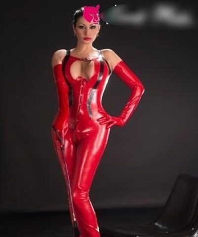 Eine Frau in einem glänzenden roten Latex-Bodysuit und High Heels steht neben einem schwarzen Stuhl vor einem dunklen Hintergrund. Ihr Gesicht ist teilweise verdeckt.